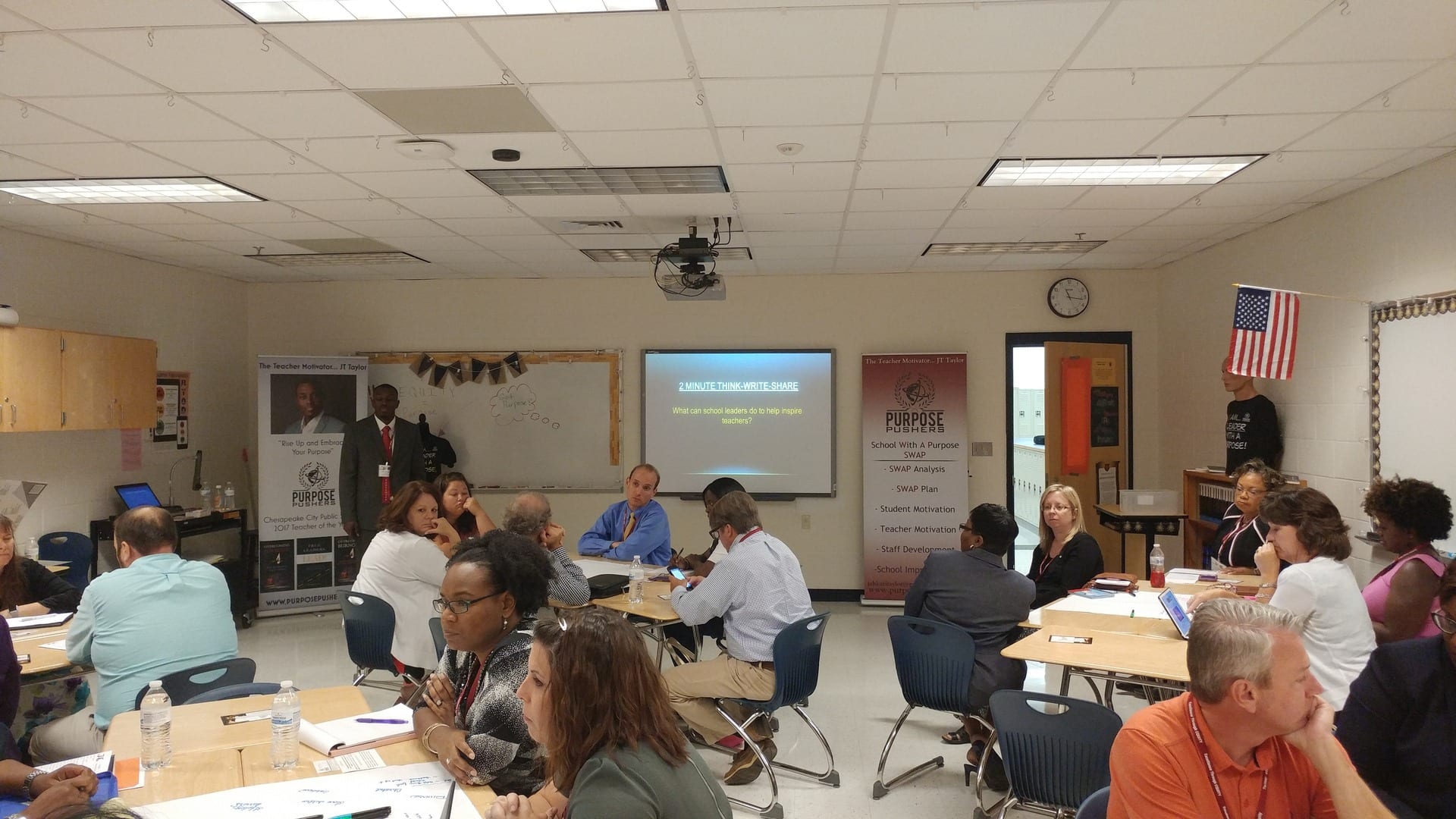 A group of people sitting at tables in front of a projector screen.